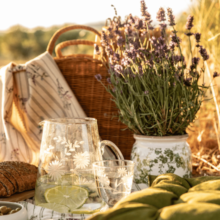 De la lavande dans un vase à motifs posée sur l'herbe avec un pichet et un panier en osier