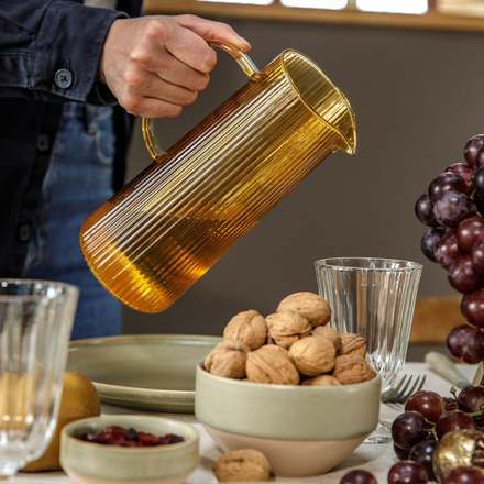 Un homme qui tiens une carafe d'eau et un bol de noix posé sur la table