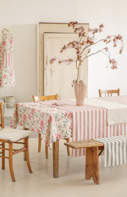 Table au couleur douce et fleuri avec une nappe rayée, des torchons, des chaises et un banc