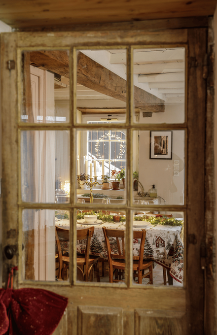 Une table de Noël dans une ambiance rustique et conviviale vue à travers une porte vitrée en bois