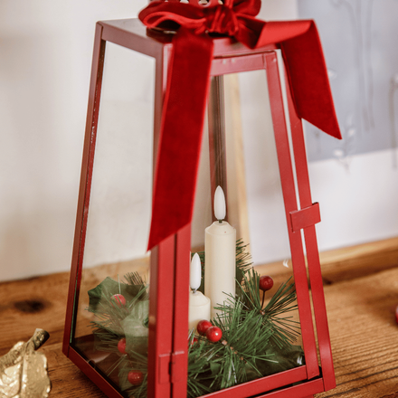 Un photophore rouge décoré avec un branchage artificiel et des bougies pour noël