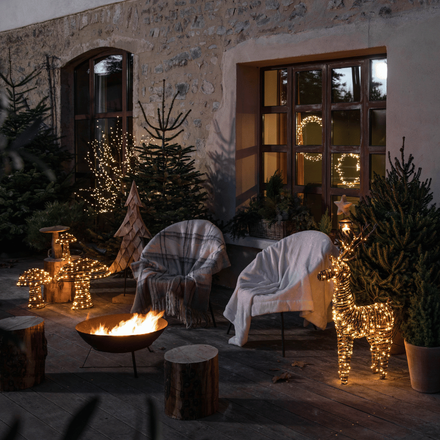 Un extérieur de Noël avec des fauteuils éclairés par un feu de bois et des lumières en forme de renne et champignons