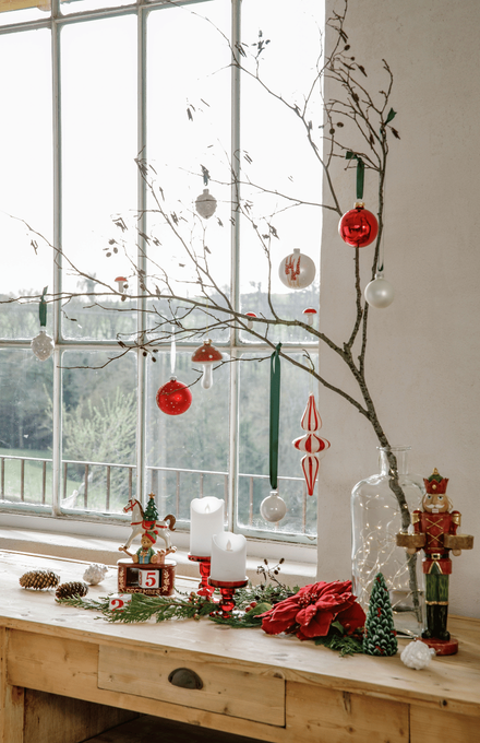 Un meuble avec des bougies et une branche d'arbre avec des boules de Noël rouges et blanches