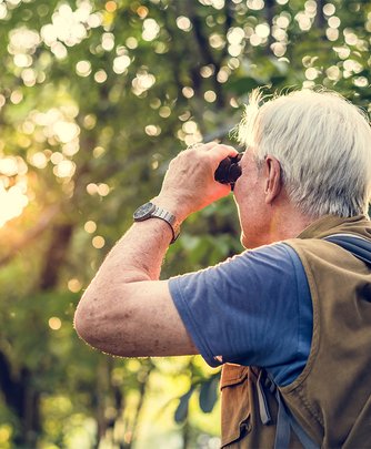 Un homme qui observe les oiseaux du jardin grâce à une paire de jumelles