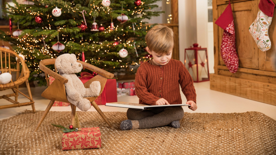 Un enfant qui lit une histoire au pied du sapin