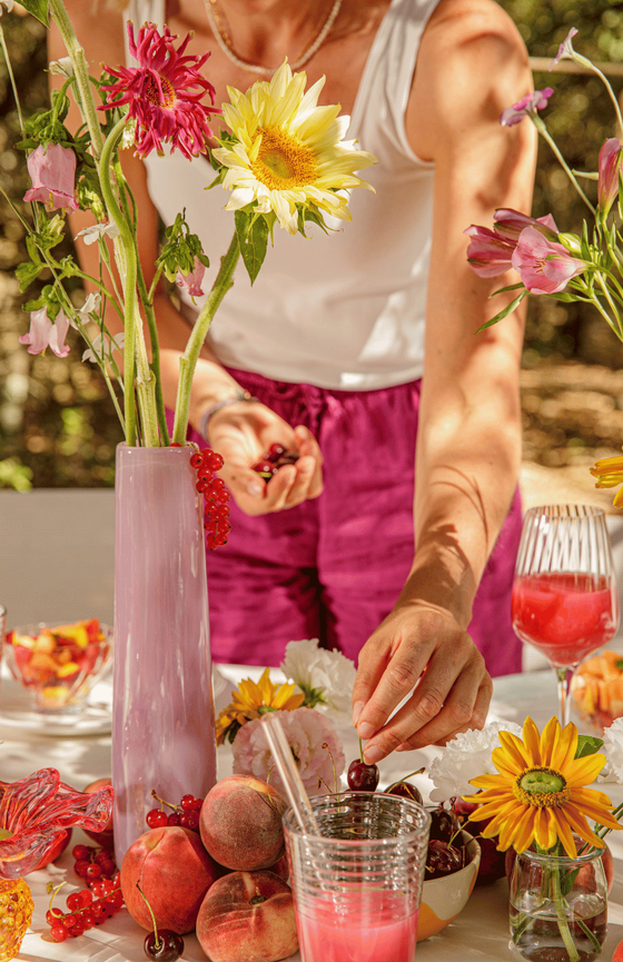 Sur une table d'été colorée et fleurie, une femme qui prend une cerise dans ses doigts