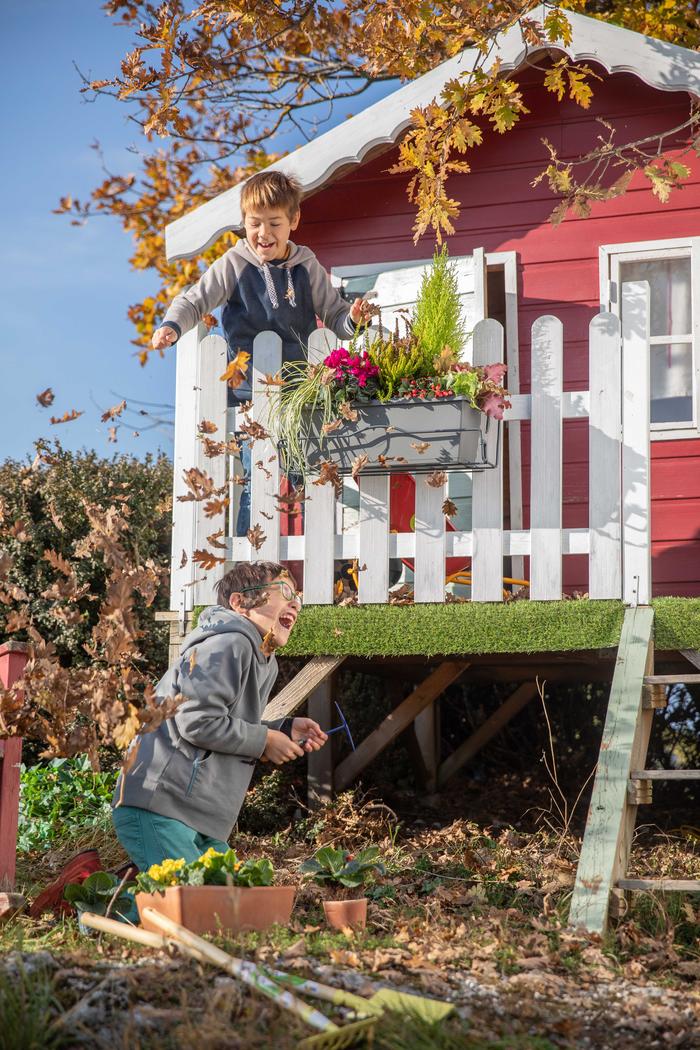 Enfants qui jouent dans une cabane rouge en automne avec les feuilles mortes